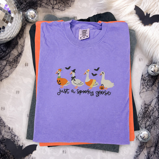 purple comfort color t-shirt with a 'just a spooky goose' embroidered design featuring four halloween costume decorated geese and bats, 